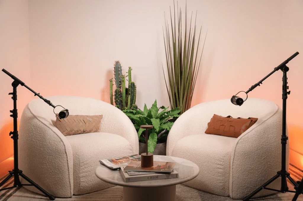 Beige chairs and boom microphones in a softly lit podcast recording set